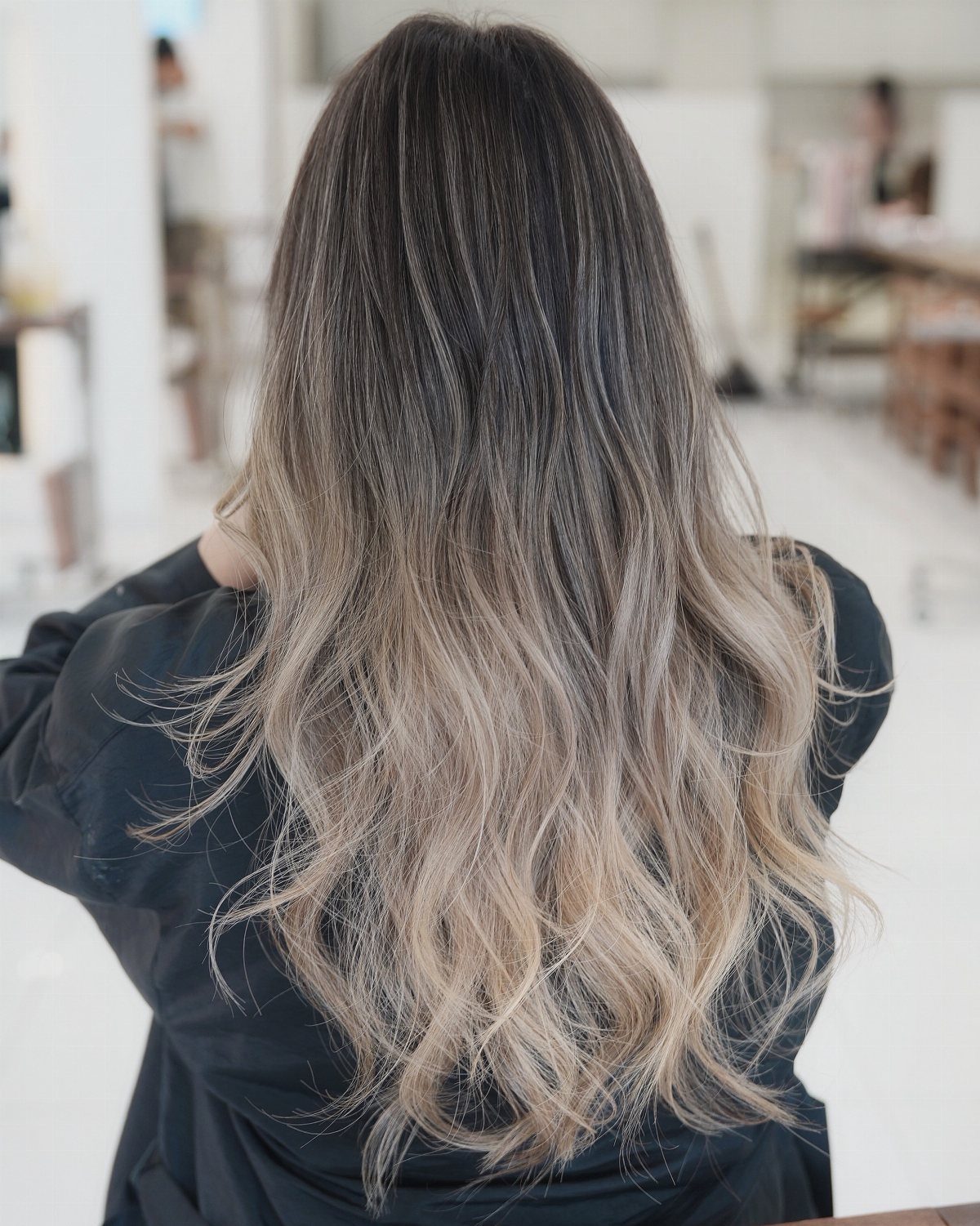 Long wavy hair fades from dark roots to cool ash blonde ends