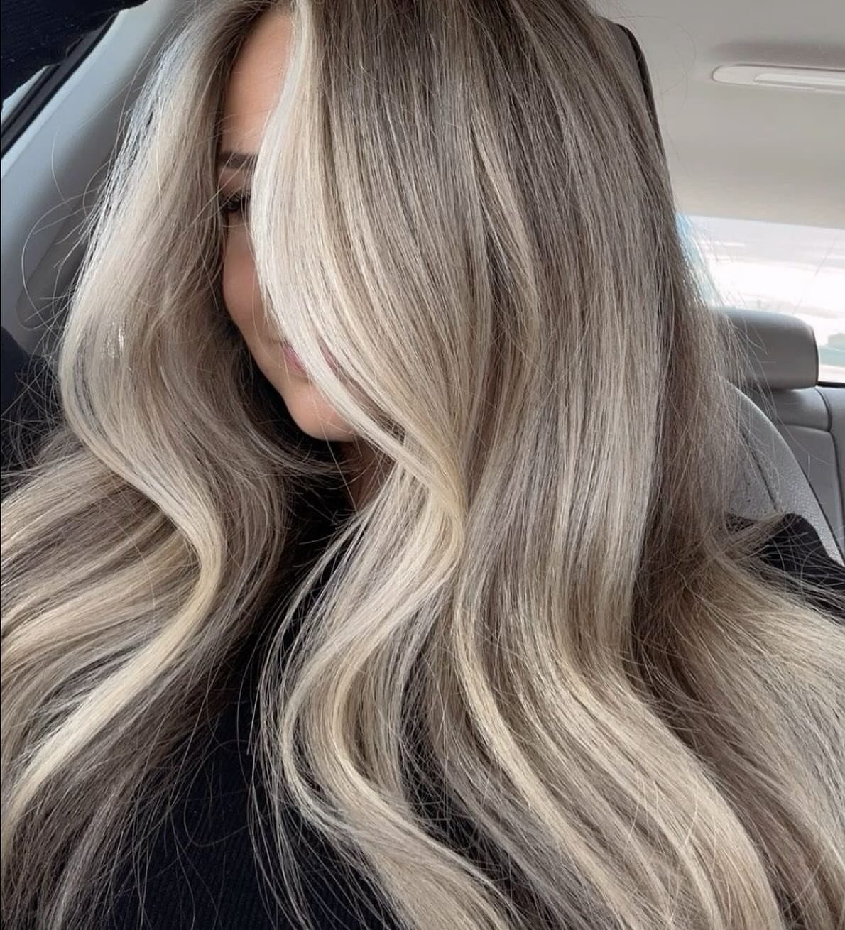 Long wavy ash-blonde hair with darker roots, photographed inside a car