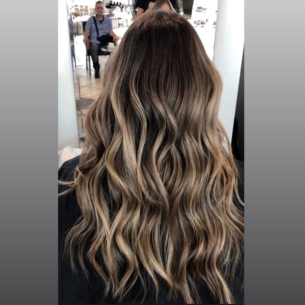 Long dark ash blonde waves with hand-painted pale highlights in a salon