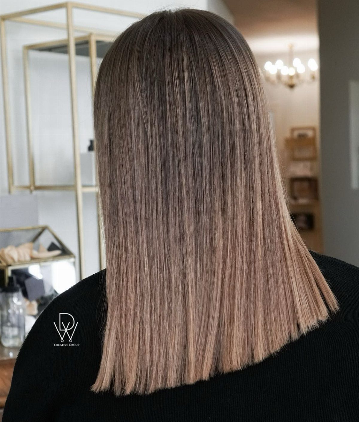 Straight shoulder-length ash blonde balayage with darker roots in a salon