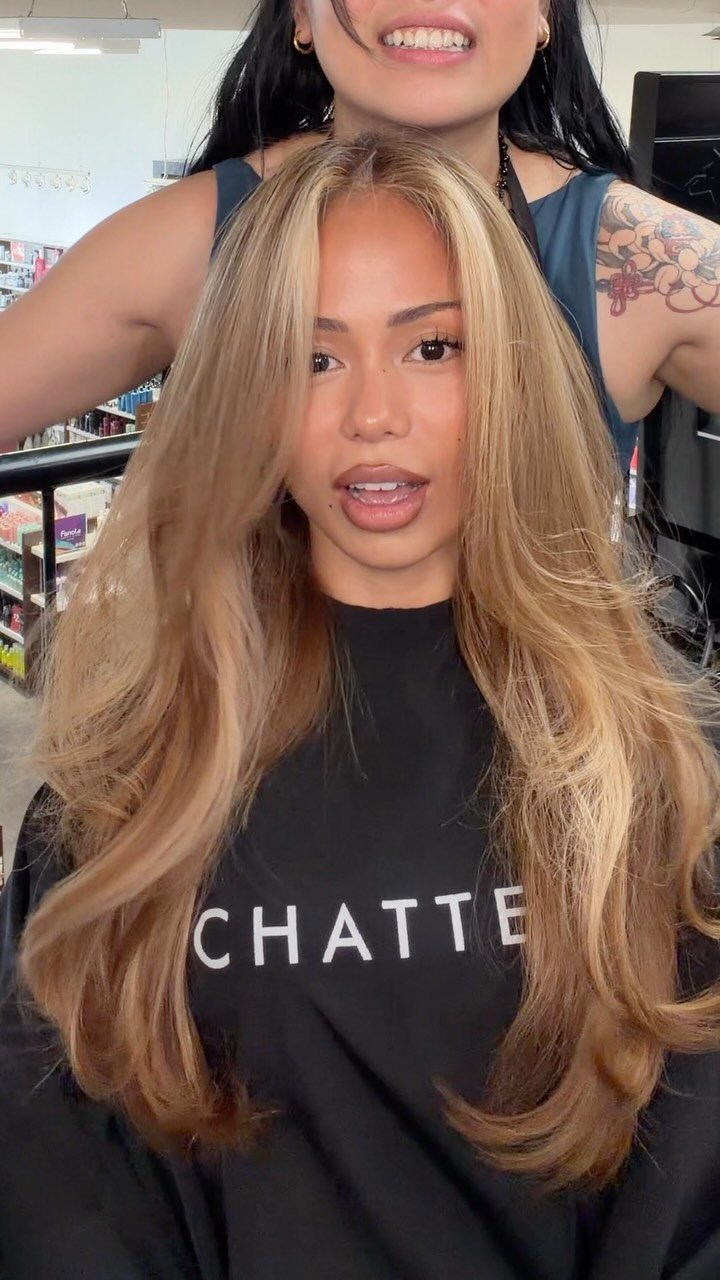 Long honey-blonde layered hair with darker roots, styled around a woman's face