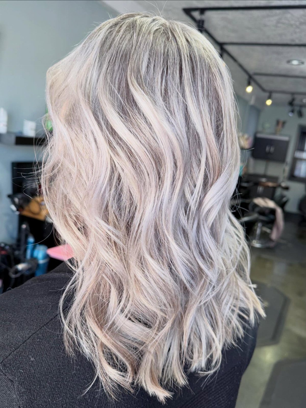 Long, wavy icy ash blonde hair shown from behind in a salon