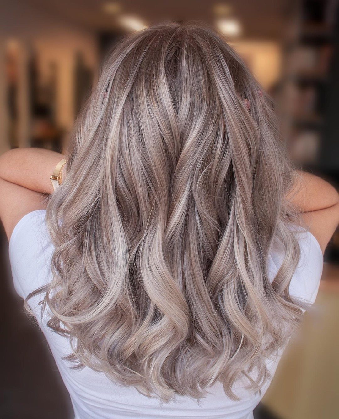 Long pale ash-blonde hair styled in loose waves over a white top