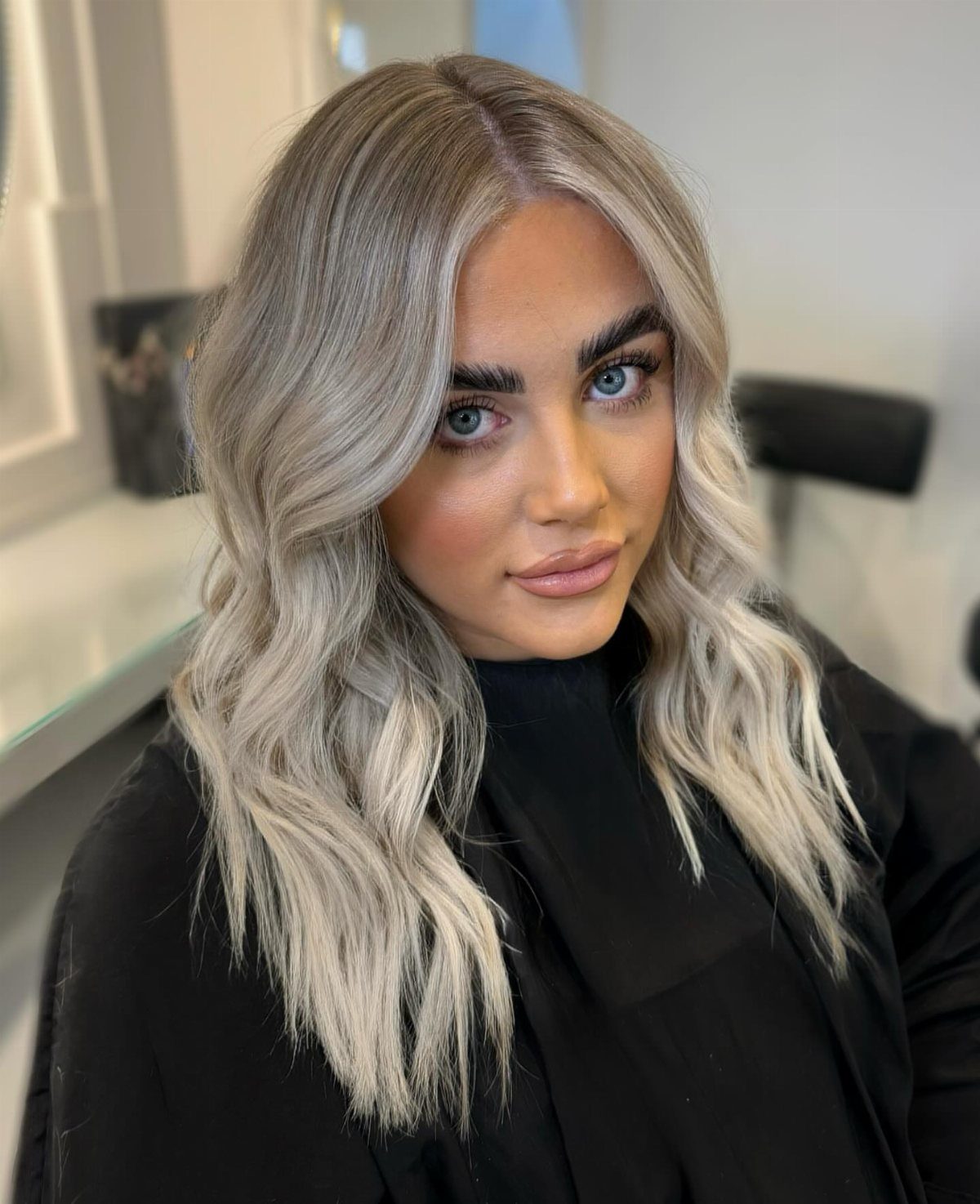 Woman with platinum ash blonde waves and dark roots in a salon