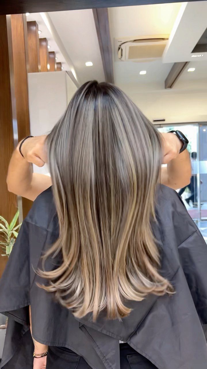 Long wavy ash blonde balayage with silver tones and darker roots in a salon