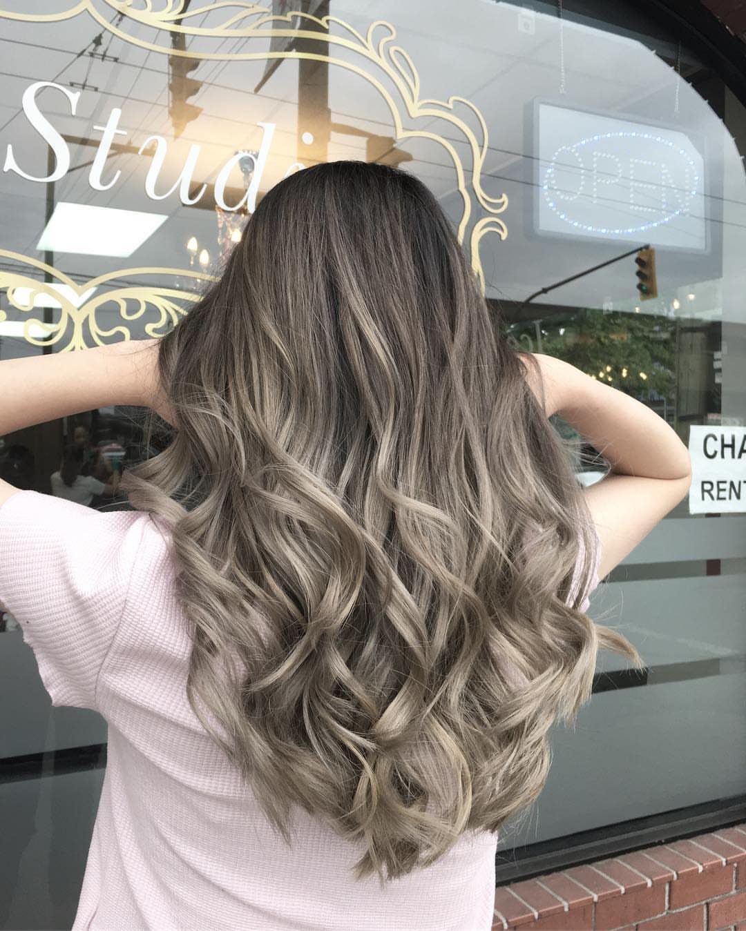 Long wavy hair fades from dark roots into cool ash-blonde ends