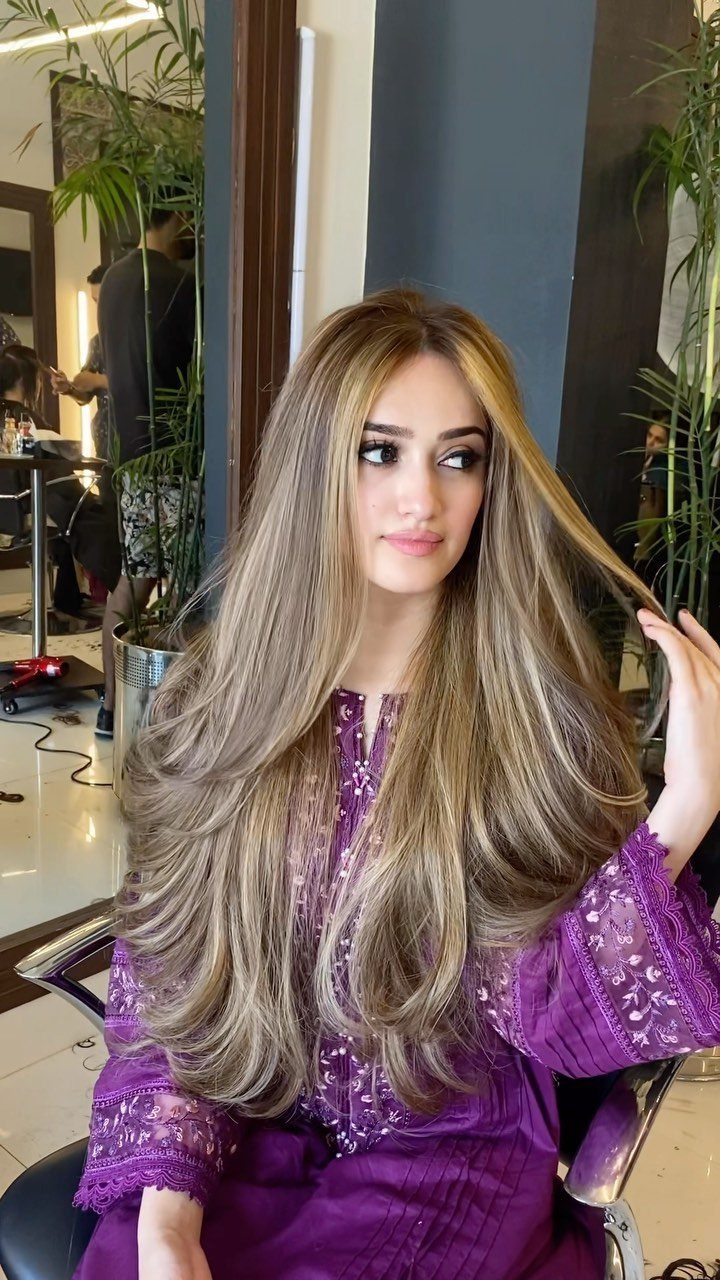 Woman displays long ash-blonde highlighted hair with darker roots in a salon