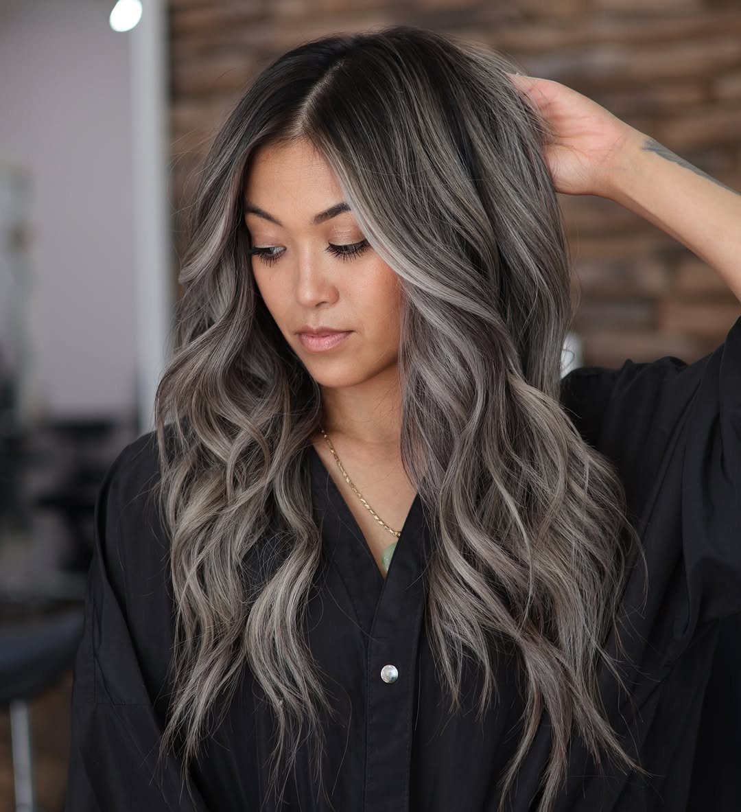 Woman displaying long wavy gray ash-blonde balayage with dark roots