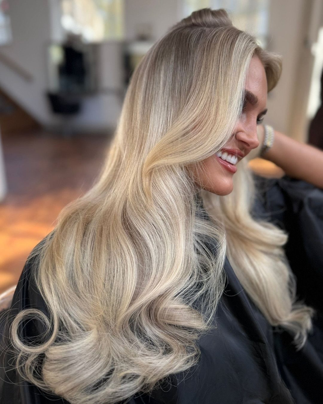 Long ash-blonde hair styled in voluminous, loose curls at a salon
