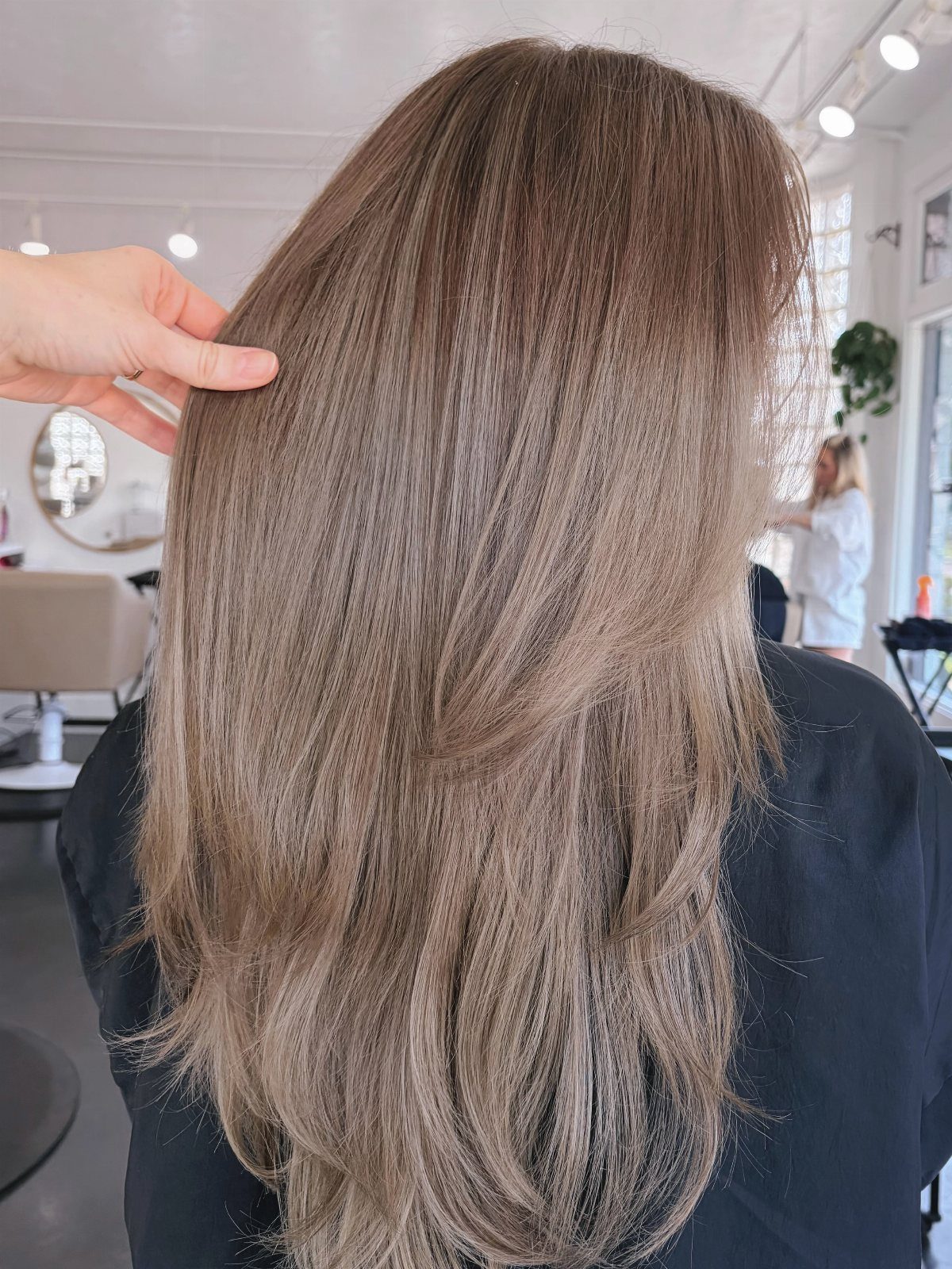 Long mushroom ash blonde hair shown from behind in a salon