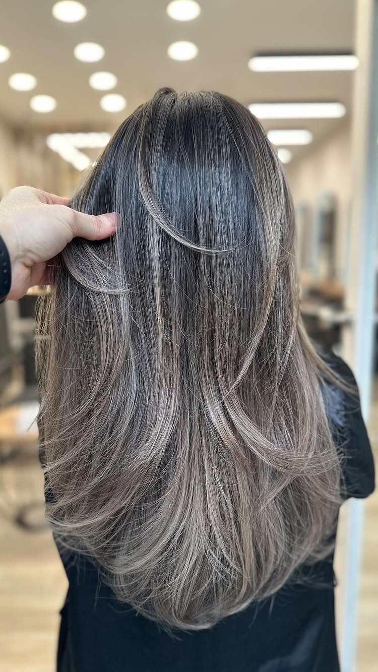 Long layered silver-gray hair with dark roots in a salon