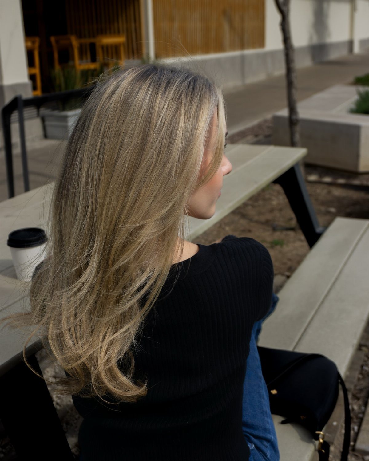 Woman with long sunlit ash blonde hair seated outdoors at a picnic table