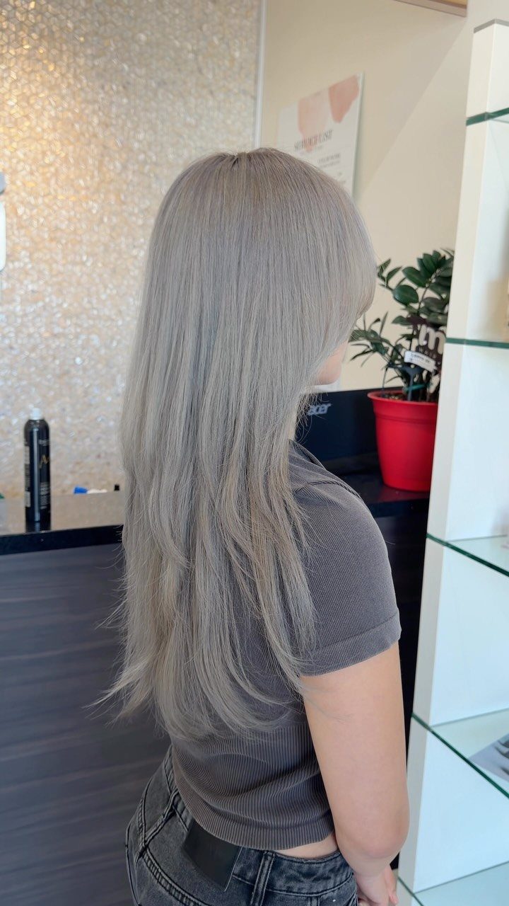 Long, cool silver-ash blonde hair falling straight down a person's back in a salon