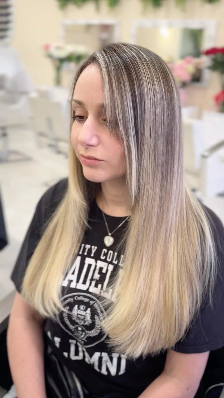 Woman displaying long, straight pale ash-blonde hair with darker roots in a salon