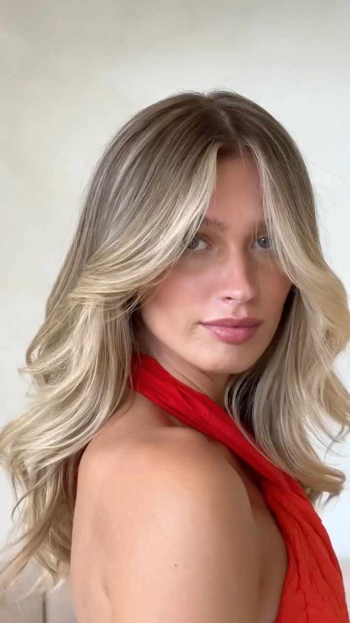 Woman with long, softly waved beige blonde hair and darker roots
