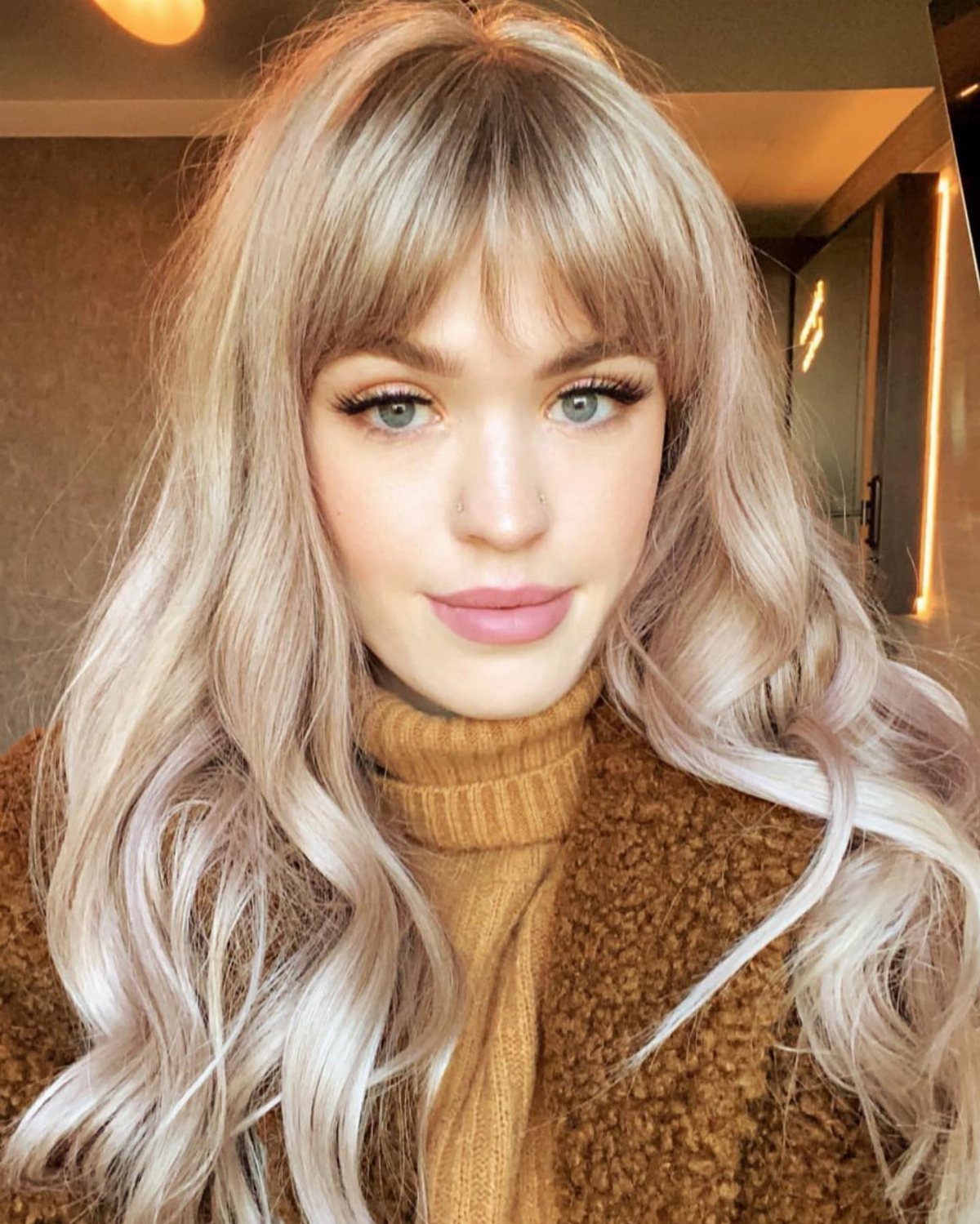 Woman wearing long beige blonde waves with wispy fringe and layered tones