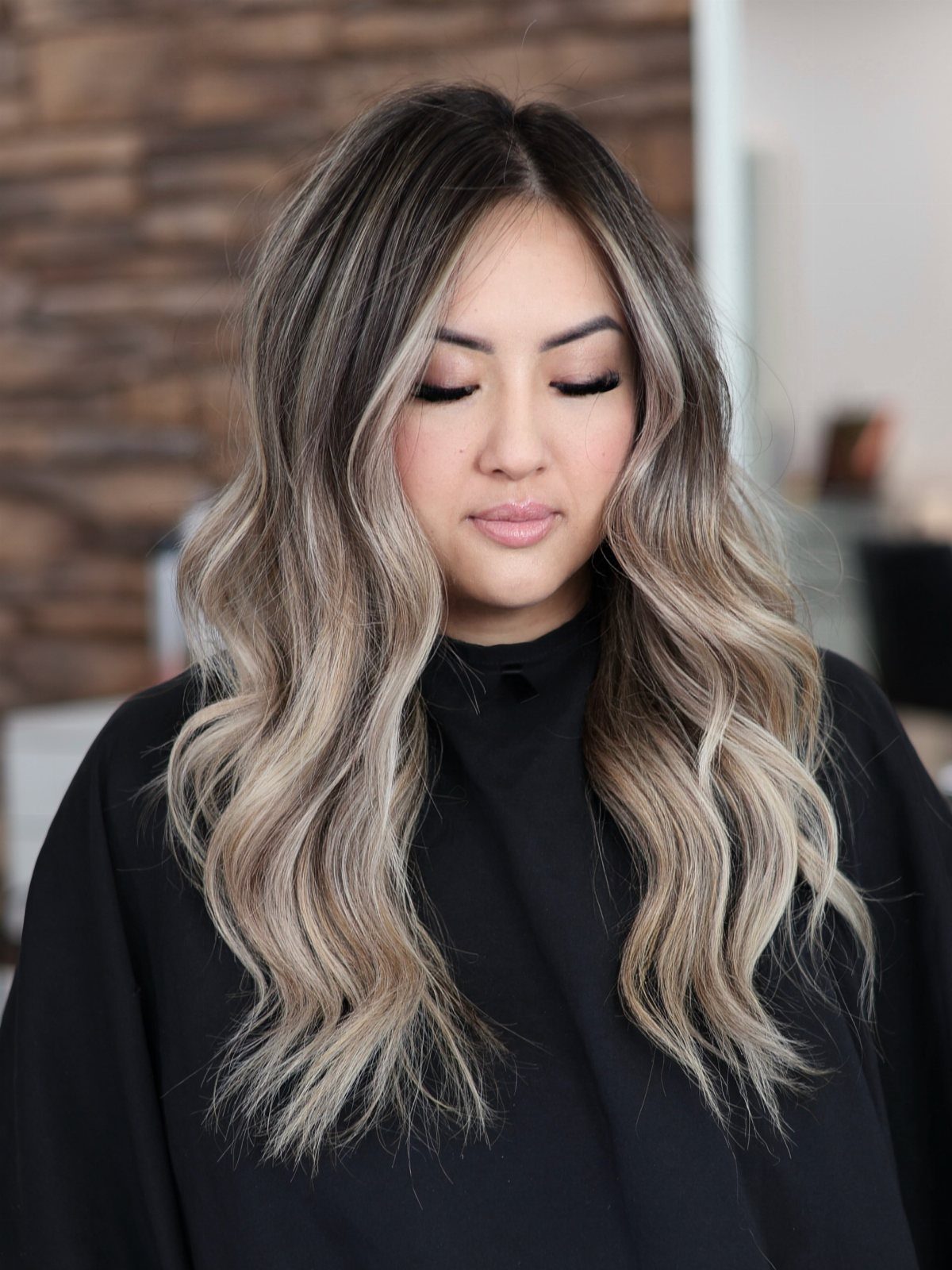 Woman displaying long wavy hair fading from dark roots to blonde ends