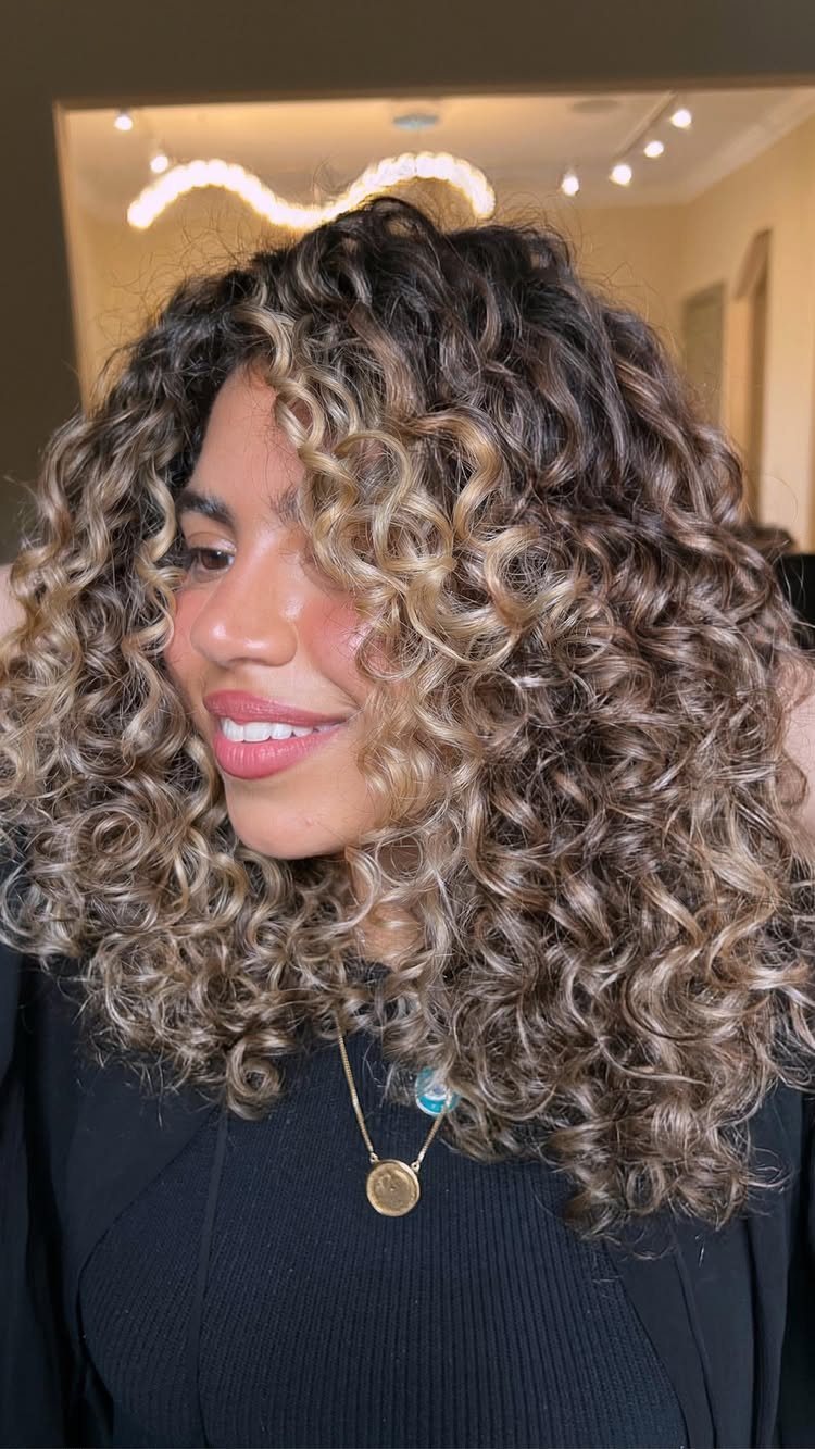 Woman with voluminous dark curls and blonde highlights wearing a black top