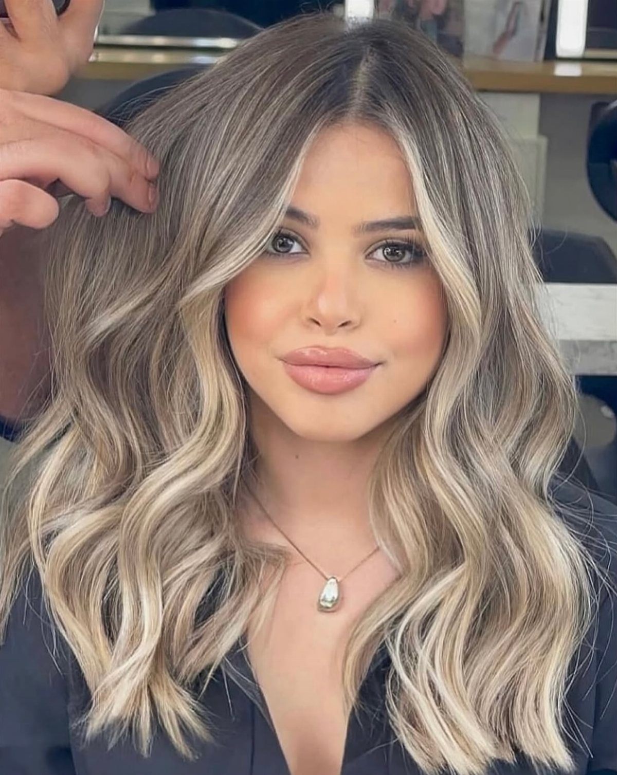 Woman displays medium beige blonde hair with long, loose waves in a salon