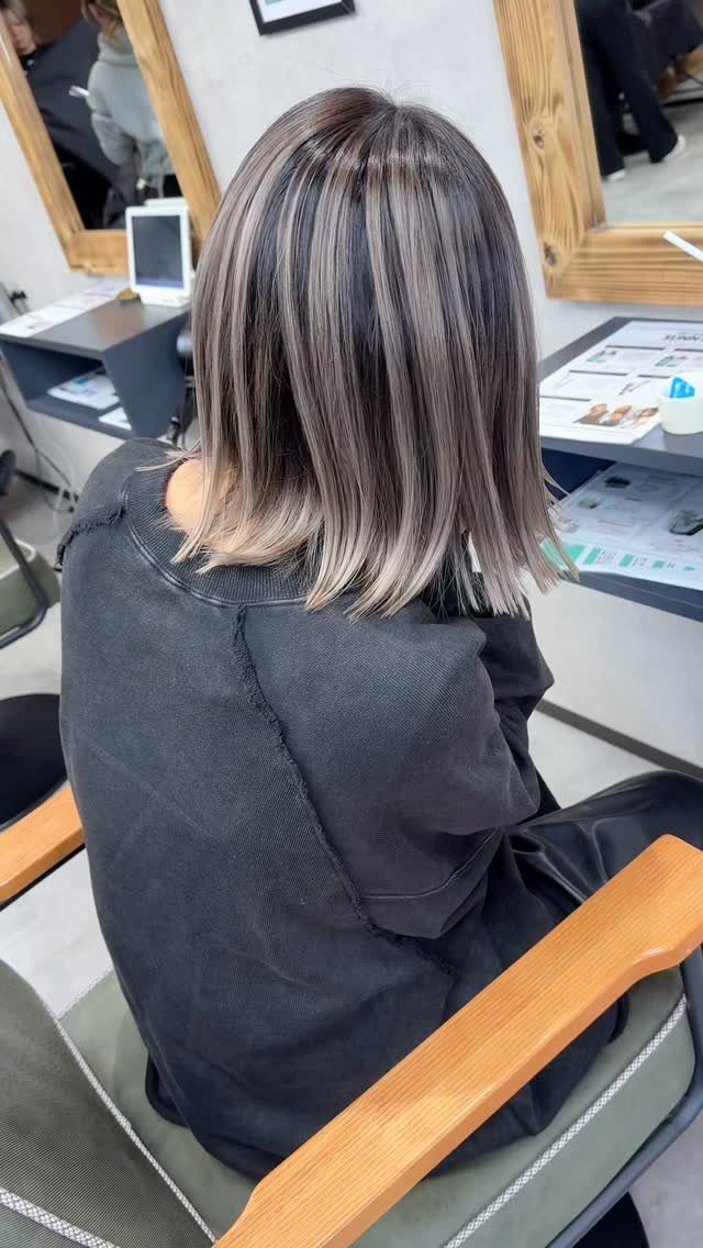 Shoulder-length dark hair with blended ash gray and pale blonde highlights in a salon