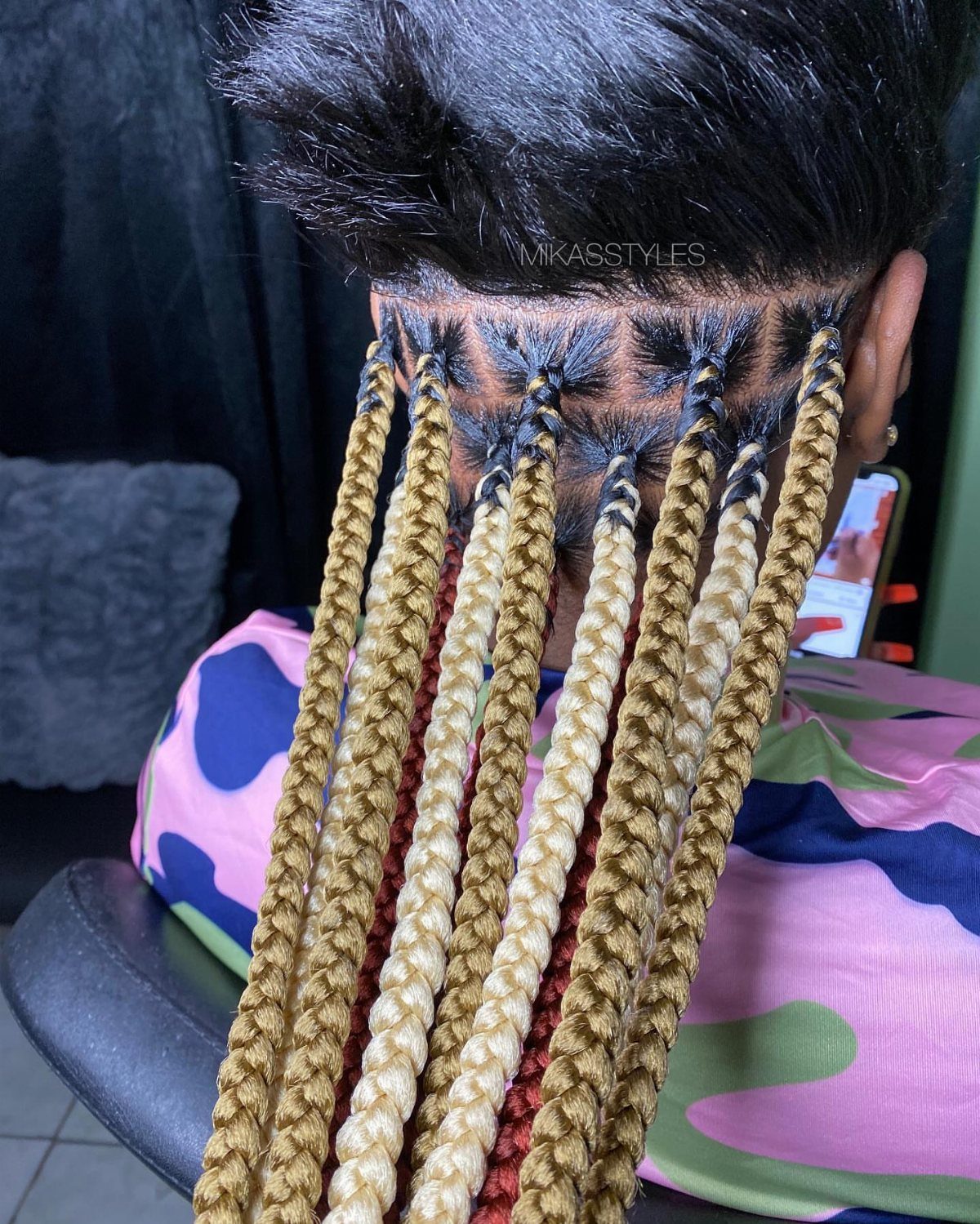 Black scalp braids woven with long blonde extensions hang down a person's back