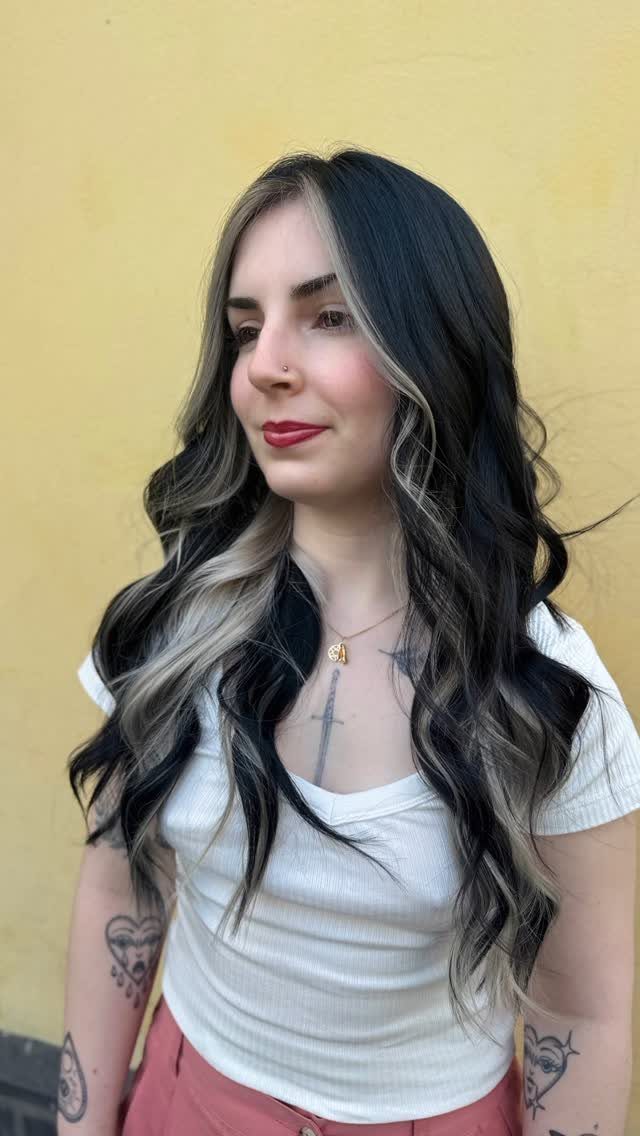 Woman with long black waves and blonde face-framing highlights against a yellow wall