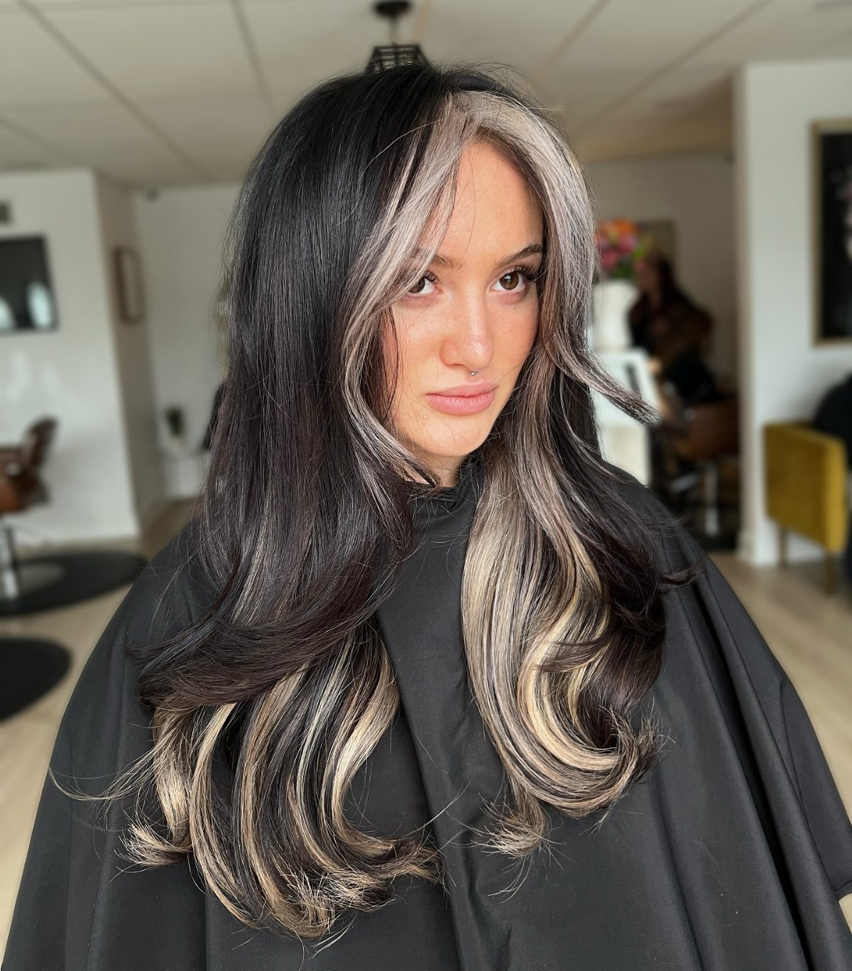 Woman with long dark hair and broad silver-blonde face-framing streaks in a salon