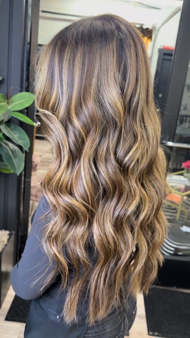 Long dark wavy hair with blended blonde balayage highlights in a salon