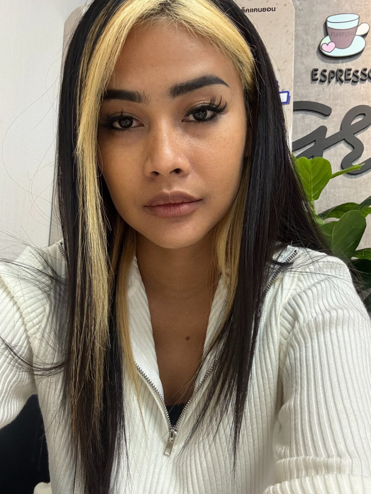 Woman with long black hair and blonde face-framing highlights wearing a white zip-up top