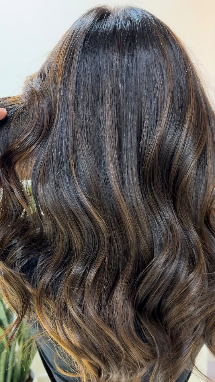Long dark hair with subtle caramel balayage highlights in loose waves
