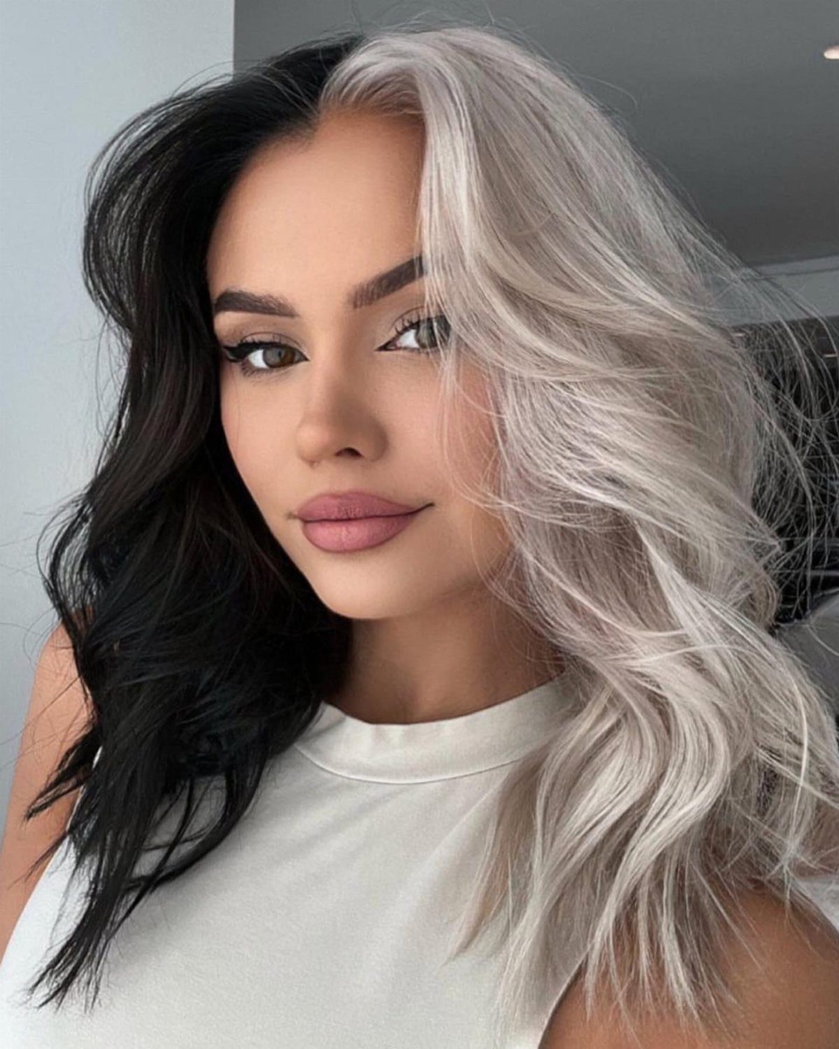 Woman with center-parted black and silver-blonde hair posing in a white top