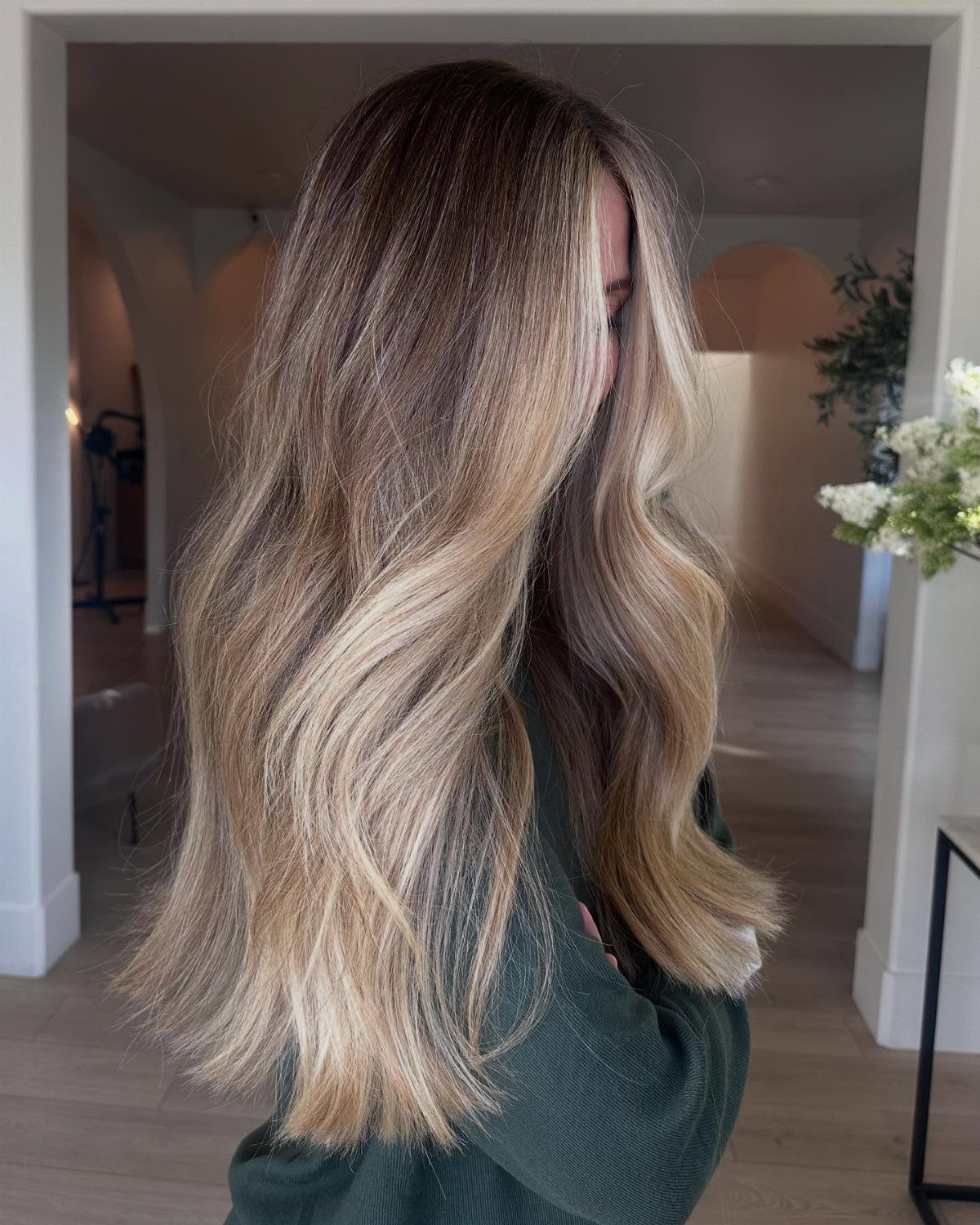 Long wavy blonde hair with dark roots, shown from the back indoors