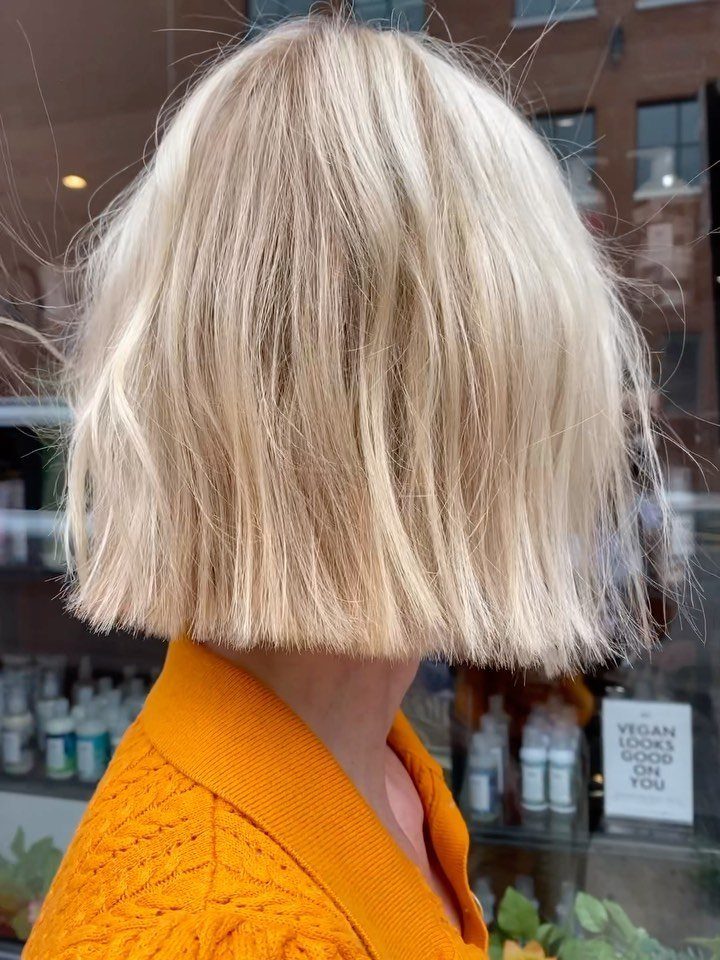 Blunt pale blonde bob with even ends above an orange sweater