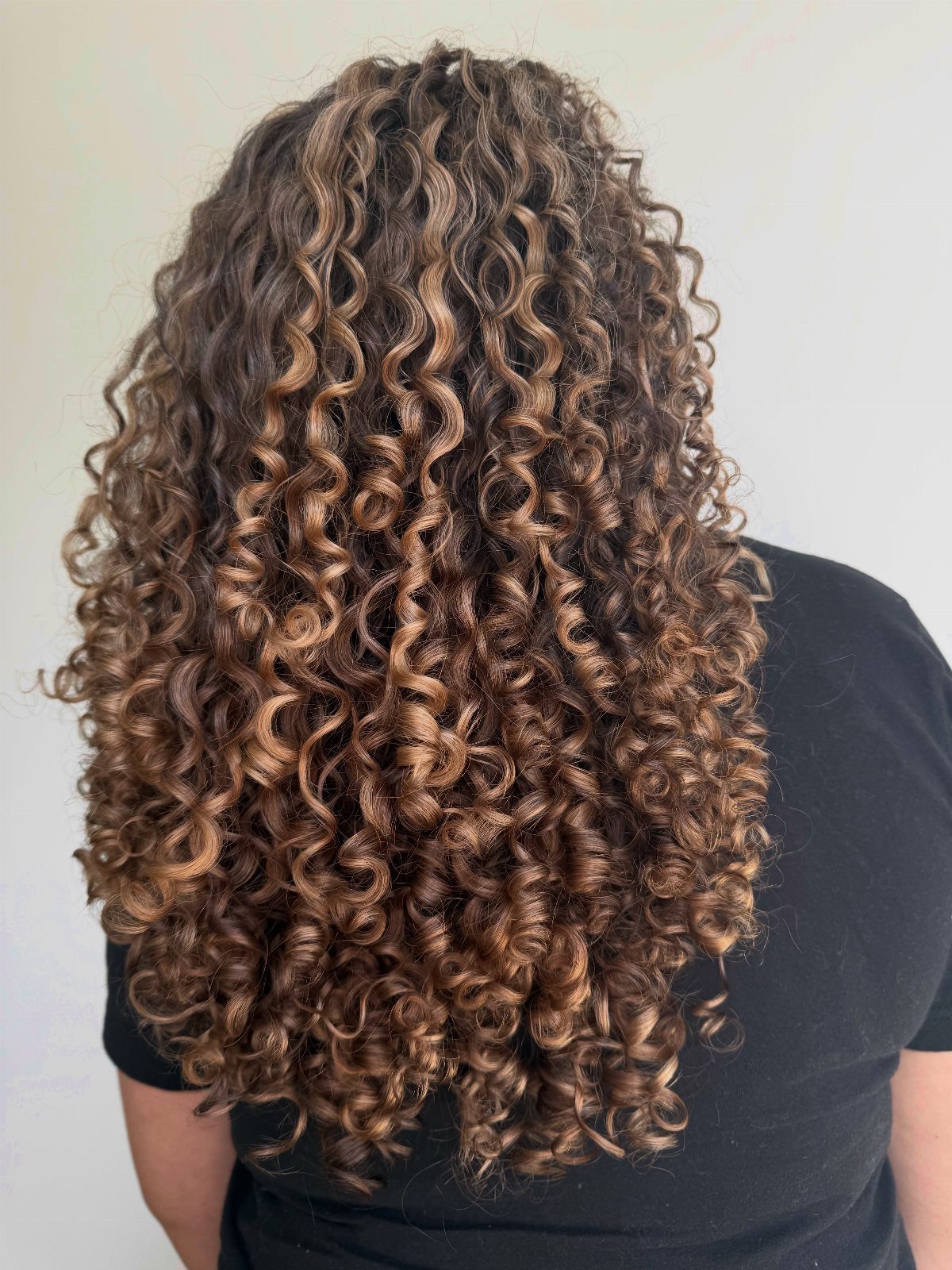 Long curly hair with golden-blonde highlights falls down the back of a person wearing black.
