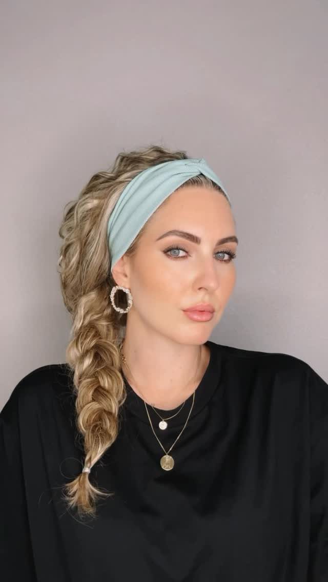 Blonde curly hair gathered into a loose side braid beneath a pale blue headband
