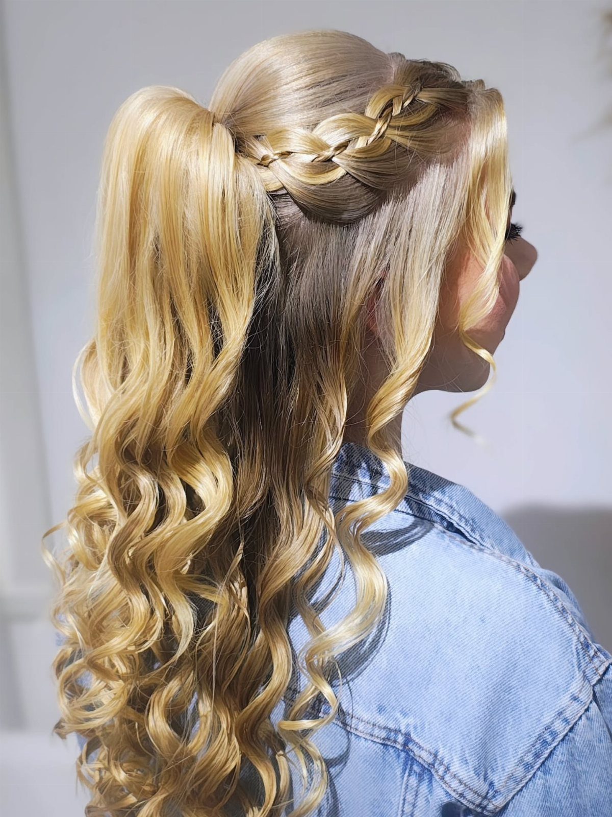Blonde curls gathered with a Dutch braid into a half ponytail