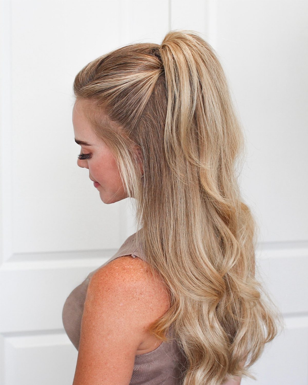 Long blonde curls fall from a high ponytail with smooth swept-back sides.