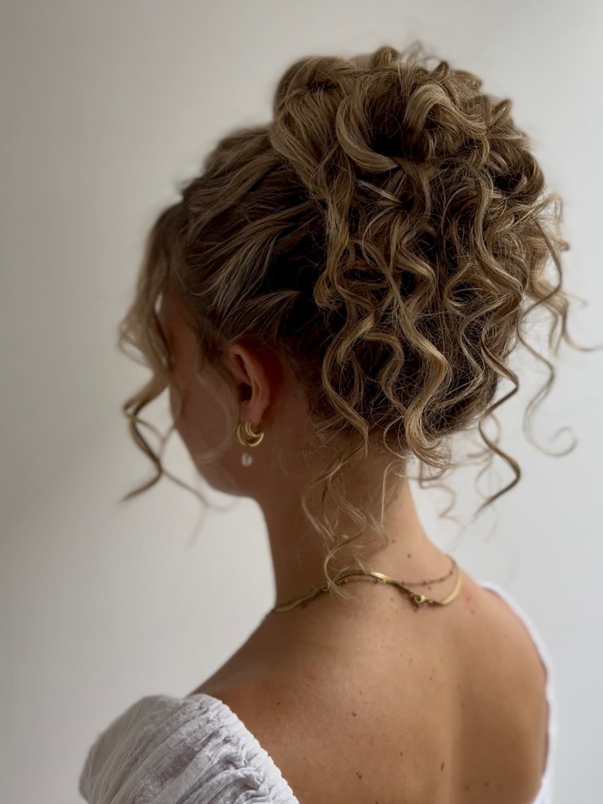 Blonde curly hair gathered in a loose updo, viewed from behind
