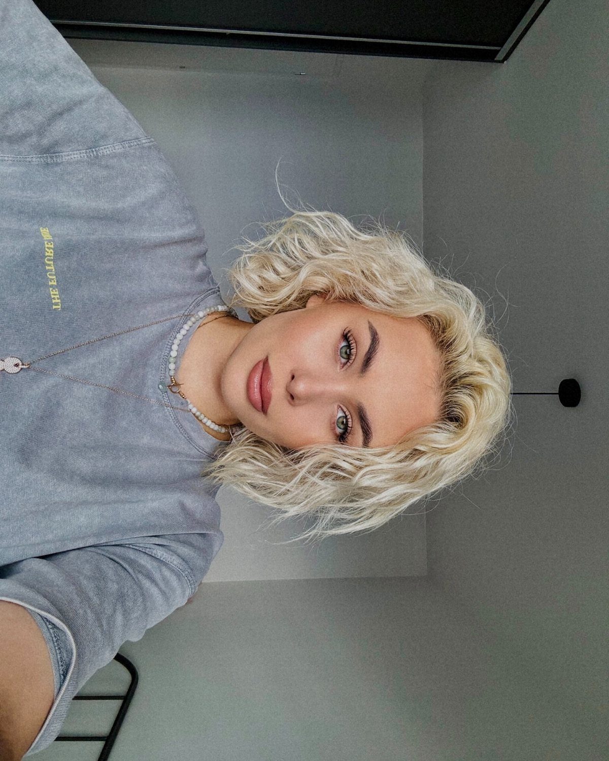 Woman with a curly golden blonde bob posing in a gray sweatshirt