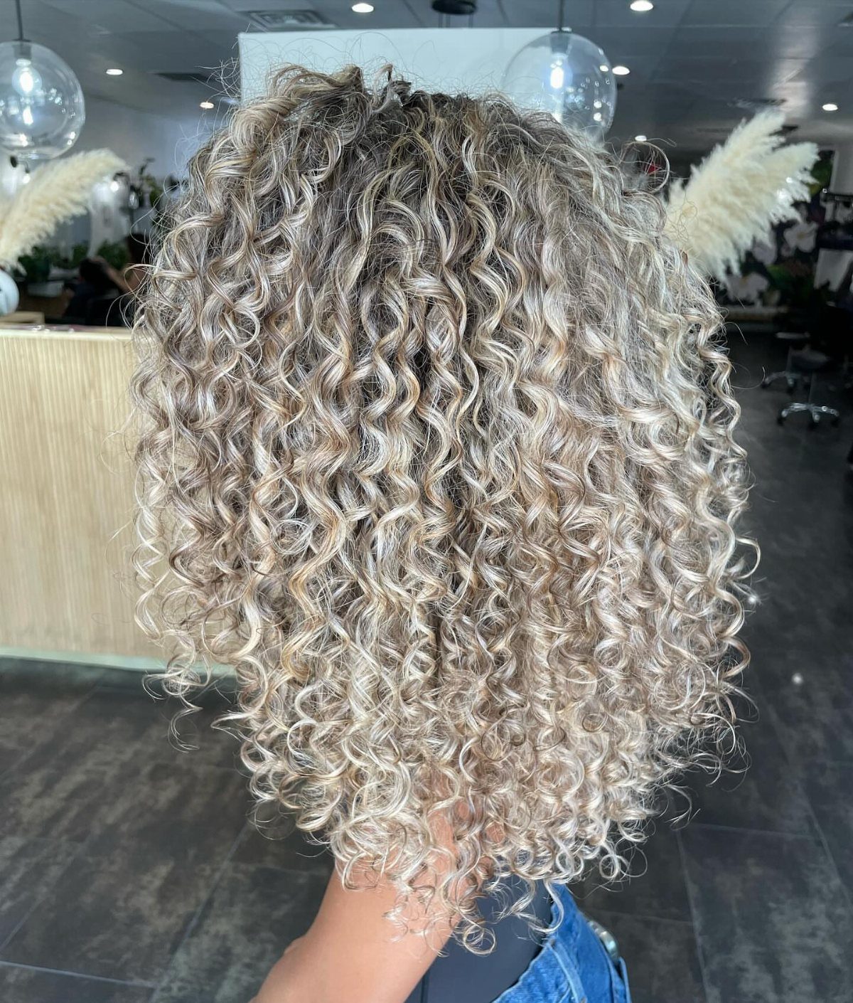 Blonde shoulder-length curls displayed from behind in a salon