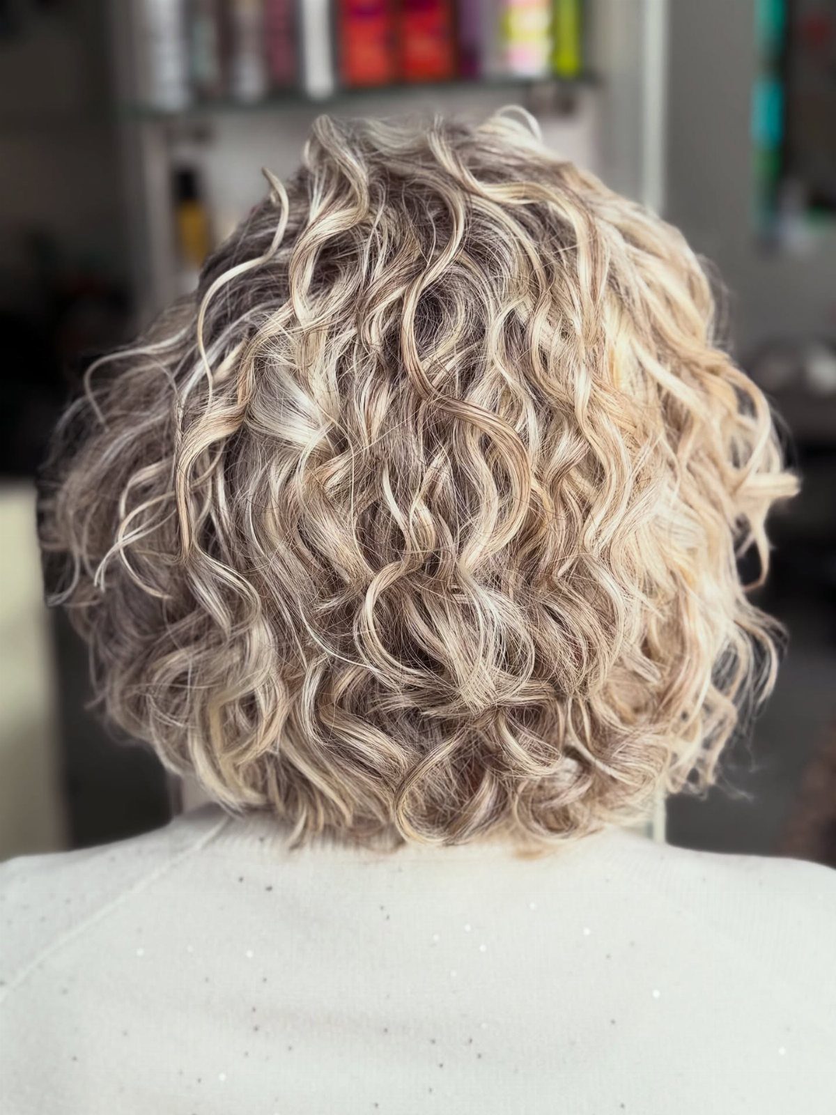 Curly bob with pale blonde highlights and darker roots in a salon