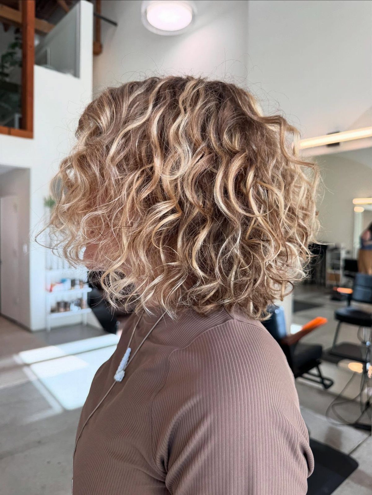 Shoulder-length blonde curls form a voluminous layered lob in a salon