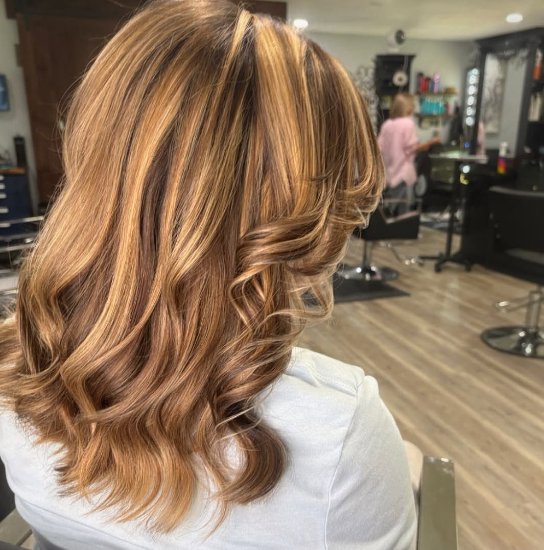 Caramel highlights brighten long, curled brown hair in a salon