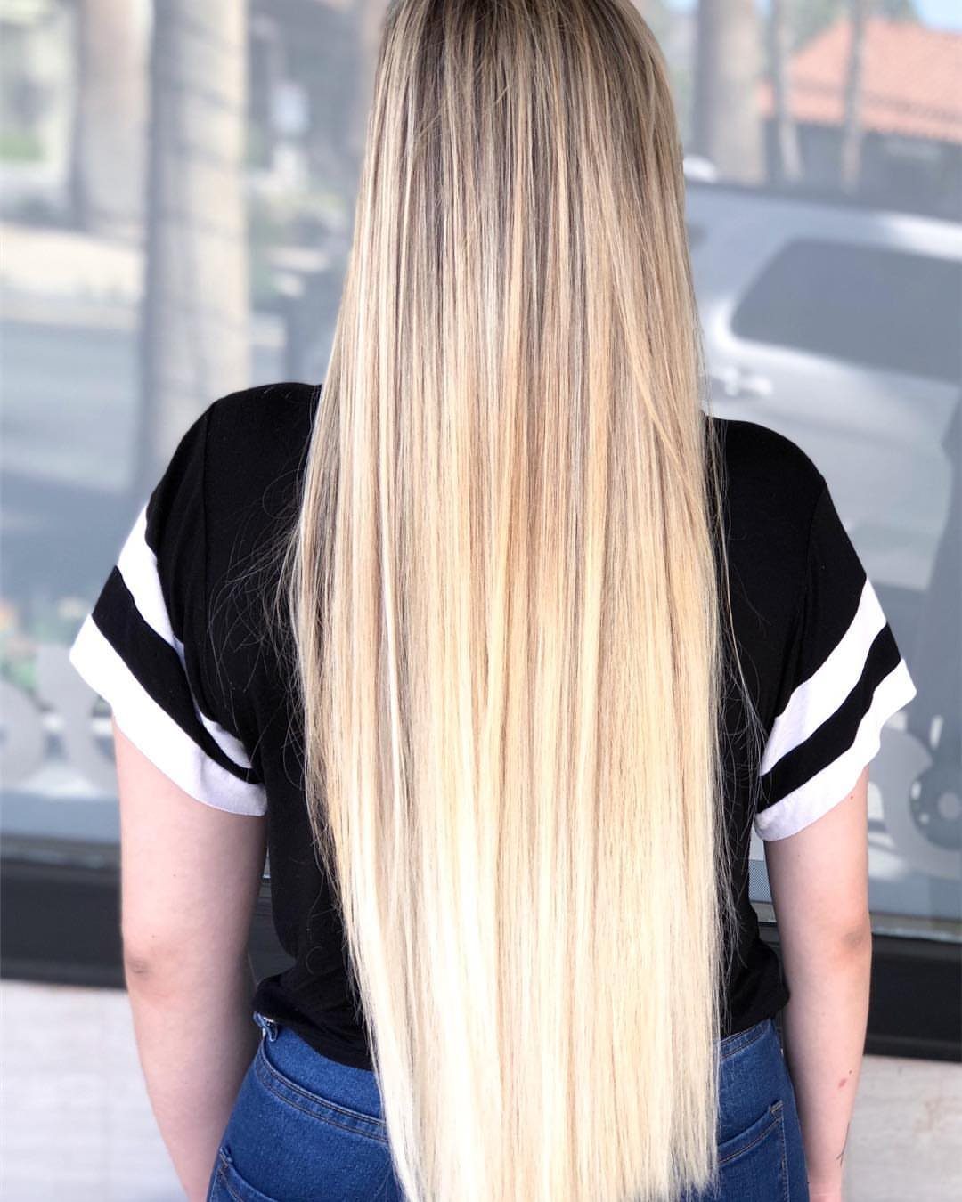 Long straight golden platinum blonde hair with dark roots falls down a person's back