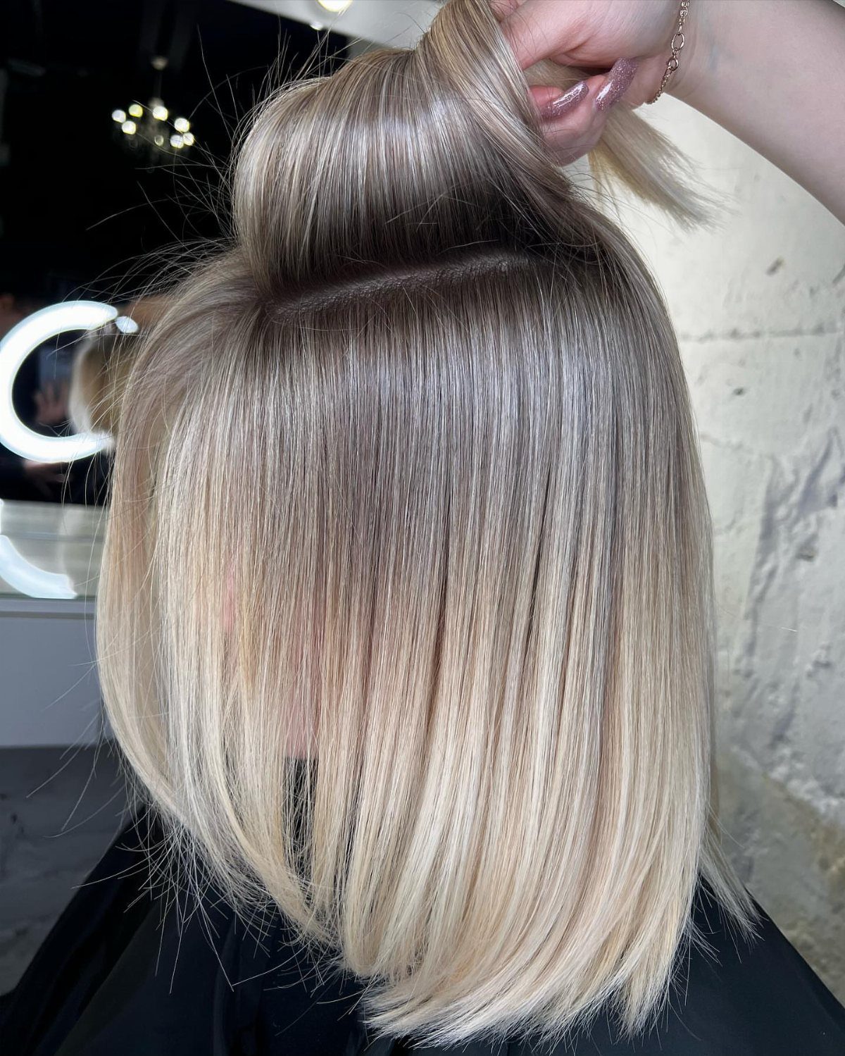Straight light beige blonde bob with dark roots shown in a salon