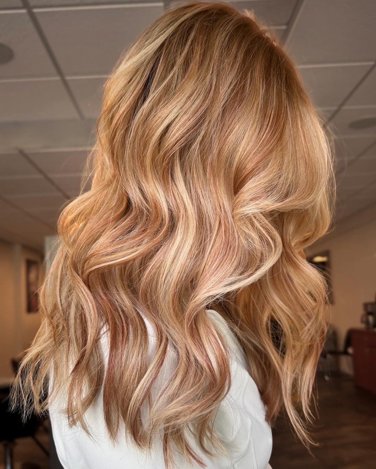 Wavy blonde hair with warm strawberry lowlights shown from behind in a salon