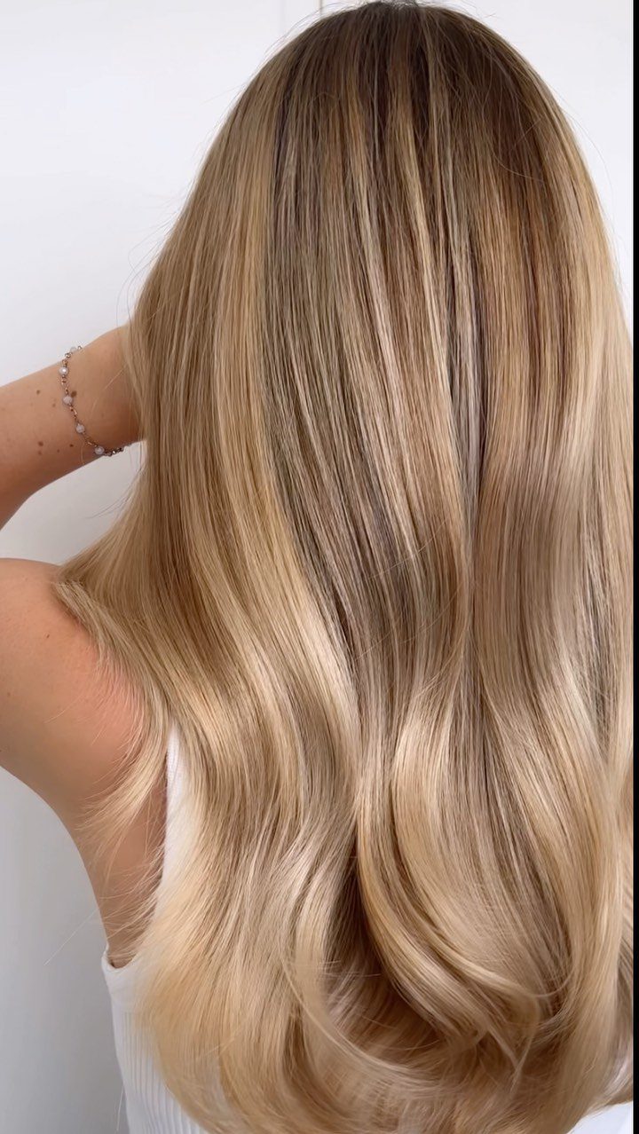Long hair blends dark roots into dimensional golden blonde balayage with curled ends