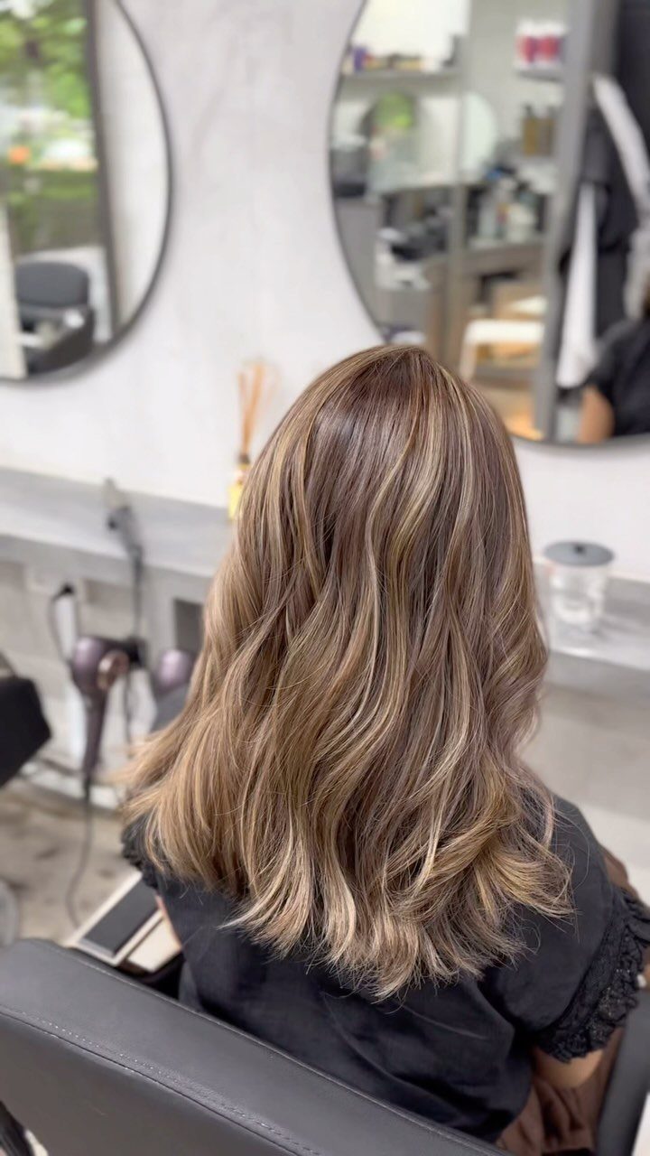 Wavy brown hair with blended cool ash-blonde highlights in a salon