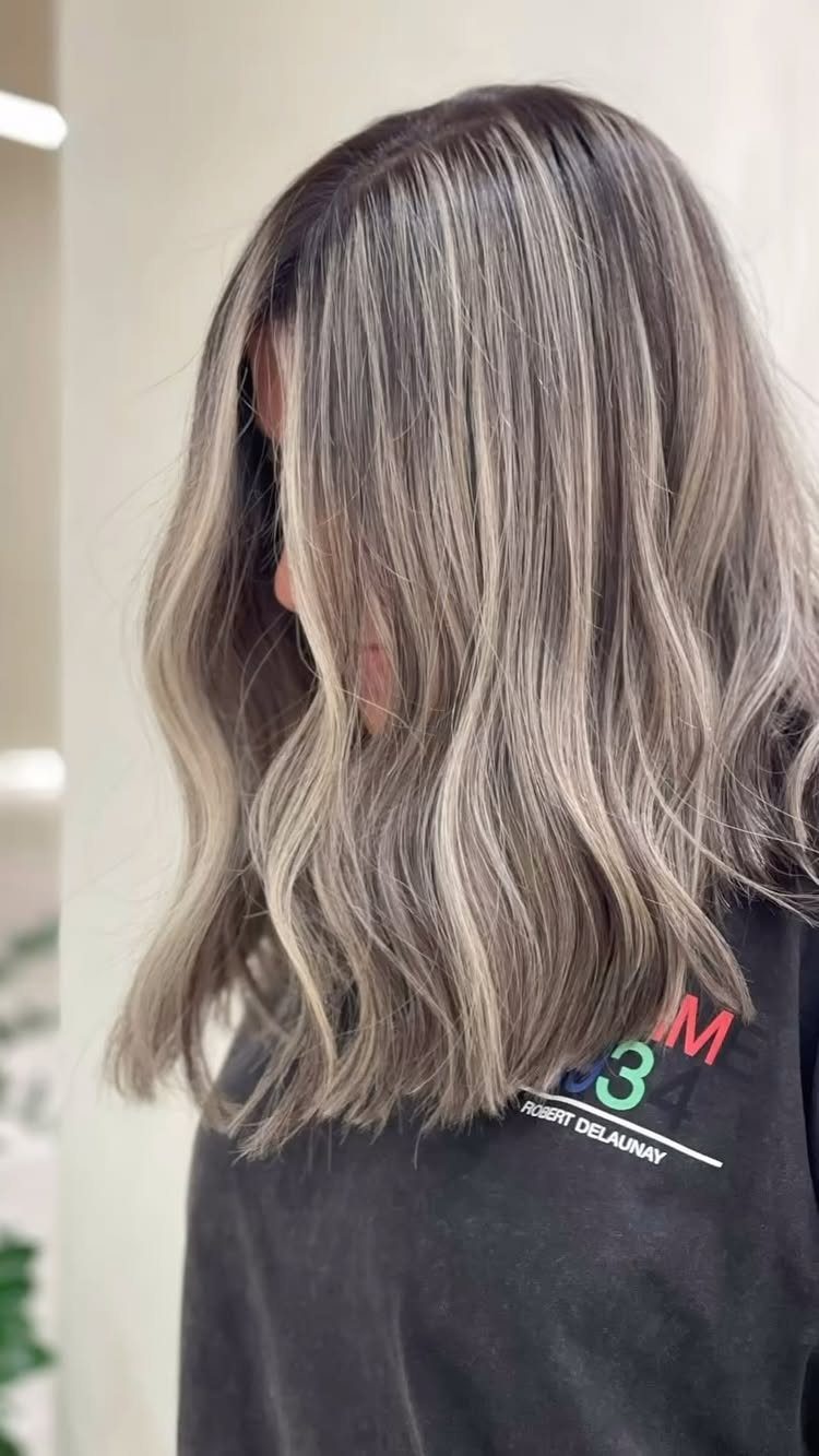 Wavy ash-blonde hair with dark roots and cool gray-beige tones