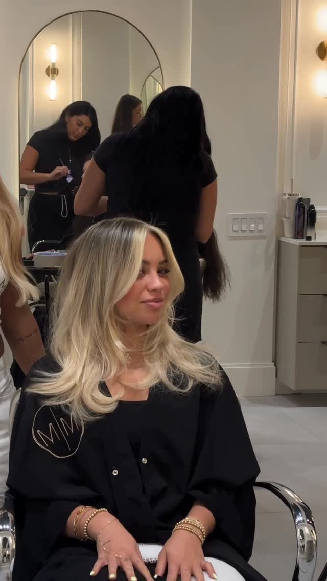 Woman with creamy blonde layered hair seated in a salon chair